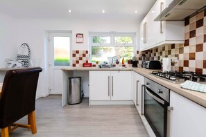 A modern kitchen with white cabinets, a stainless steel range hood, and a window with a view of greenery. - Gilfach Cynon Cottage - Beacons & BikePark (Merthyr Tydfil)