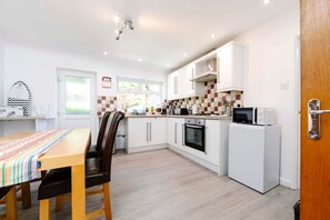 A compact kitchen with white cabinets, a microwave, an oven, and a refrigerator. - Gilfach Cynon Cottage - Beacons & BikePark (Merthyr Tydfil)