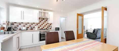 A modern kitchen with white cabinets, a checkered backsplash, and a dining area with a striped table runner.