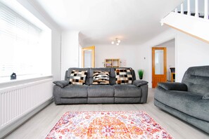 A living room with a grey sofa, patterned cushions, a colorful rug, and a wooden bookshelf. - Gilfach Cynon Cottage - Beacons & BikePark (Merthyr Tydfil)