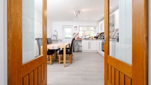 Une cuisine moderne avec des meubles blancs, un coin repas comprenant une table et des chaises, et des portes en bois.