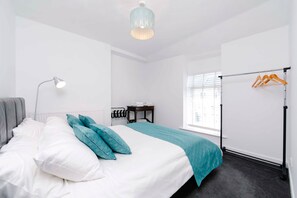 A modern bedroom with a bed, a bedside table, a hanging light, and a window with blinds. - Gilfach Cynon Cottage - Beacons & BikePark (Merthyr Tydfil)