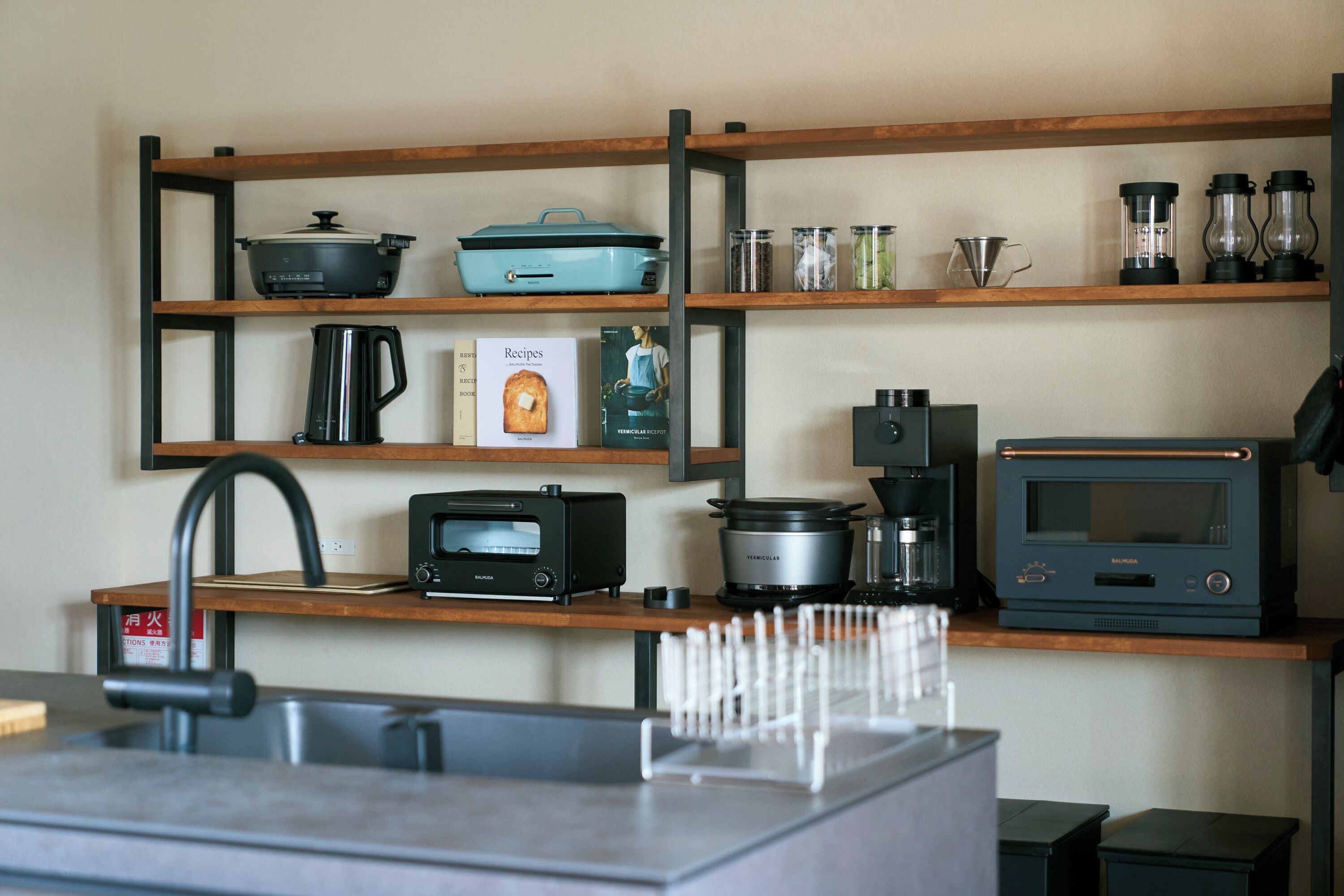 Une cuisine avec des étagères en bois, une machine à café, un grille-pain, une bouilloire, un four à micro-ondes et un livre de recettes.