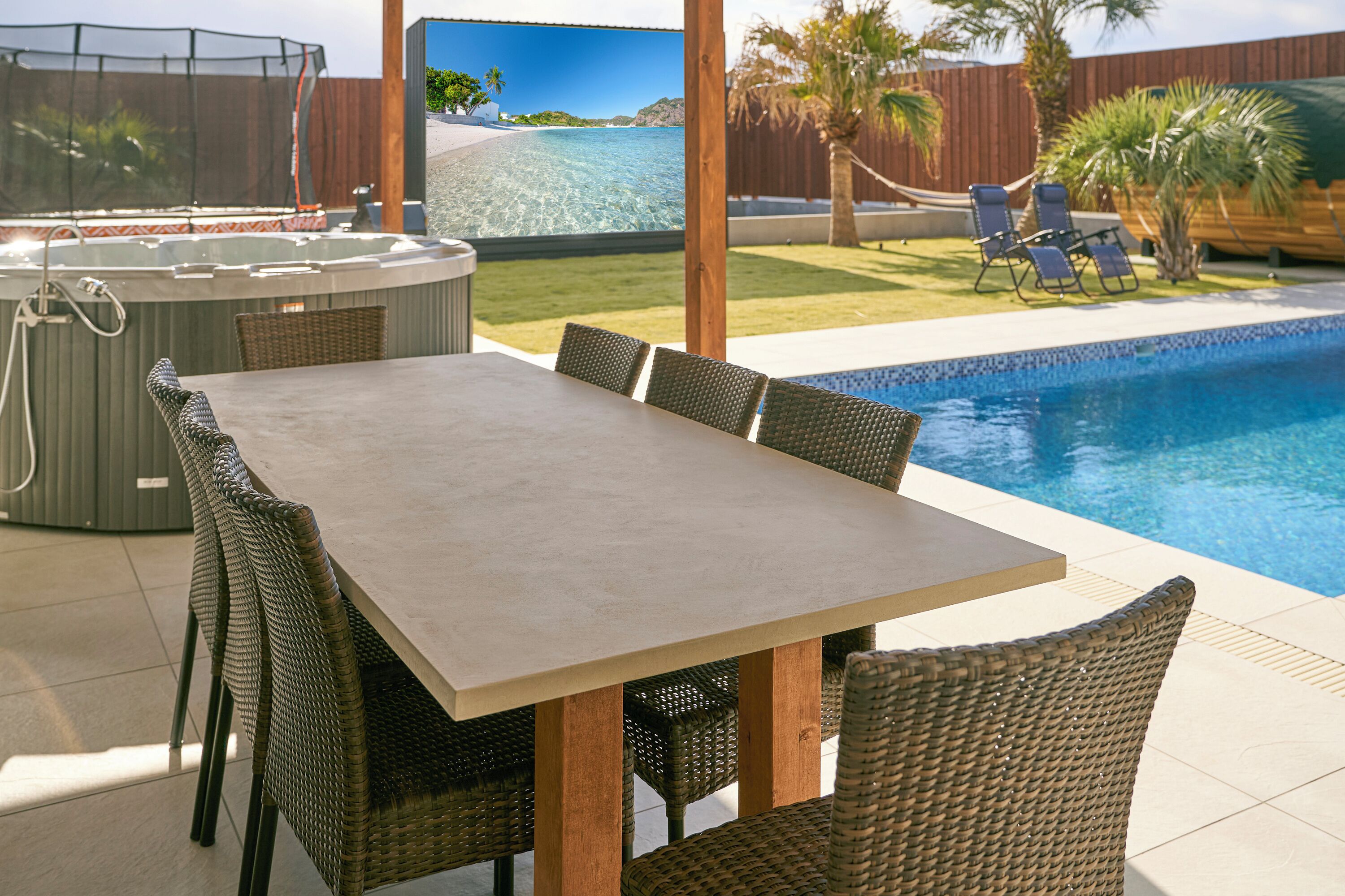 Un área de comedor junto a la piscina con mesa y sillas, un jacuzzi y vistas al océano.