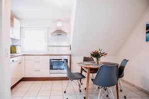 Une cuisine moderne avec des armoires blanches, un four encastré et un coin repas comprenant une table et des chaises en bois.