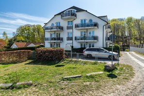 Un edificio residenziale a più piani con balconi, un'auto parcheggiata davanti e un prato ben curato.