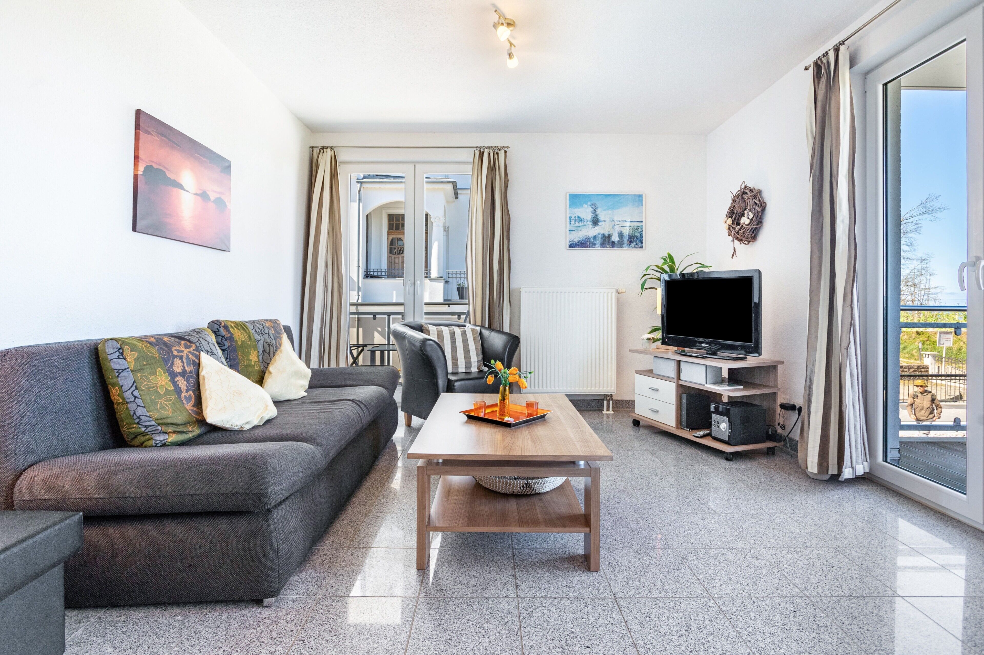 Een moderne woonkamer met een bank, salontafel, televisie en grote ramen.