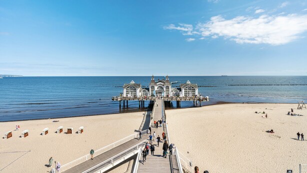 A pier leading to a building with a symmetrical facade, a sandy beach, and the ocean. - Holiday Apartment 'Am Hochufer - First Row' with Sea View, Balcony and Wi-Fi (Sellin)