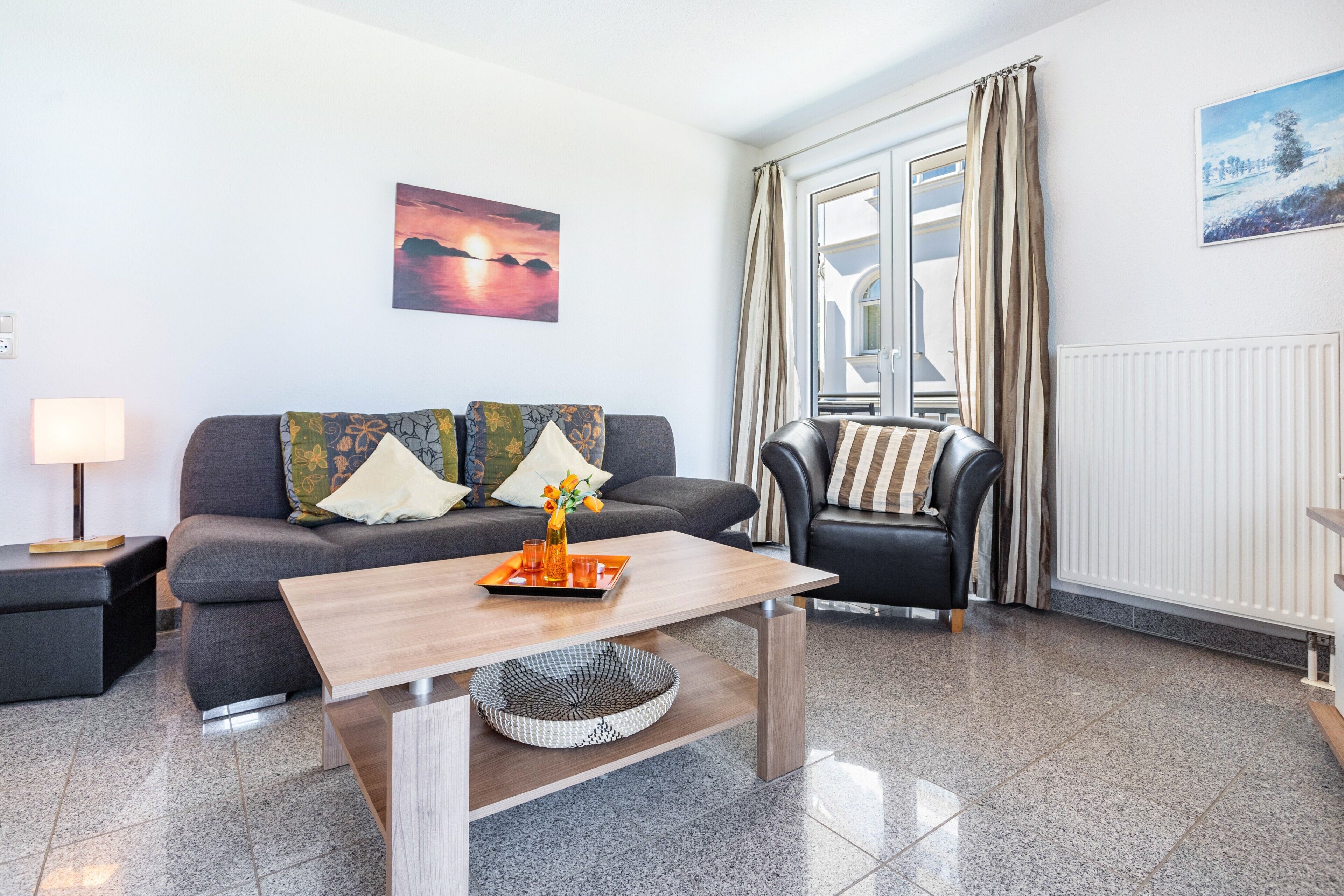 En moderne stue med sofa, sofabord, stol, lampe og et vindue med gardiner.