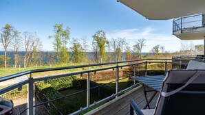 A balcony with a view of a lake and trees, a car parked outside, and a sign indicating a restaurant. - Holiday Apartment 'Am Hochufer - First Row' with Sea View, Balcony and Wi-Fi (Sellin)