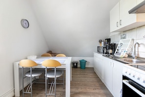 A compact kitchen with white cabinets, a stove, a sink, and a dining area with stools.