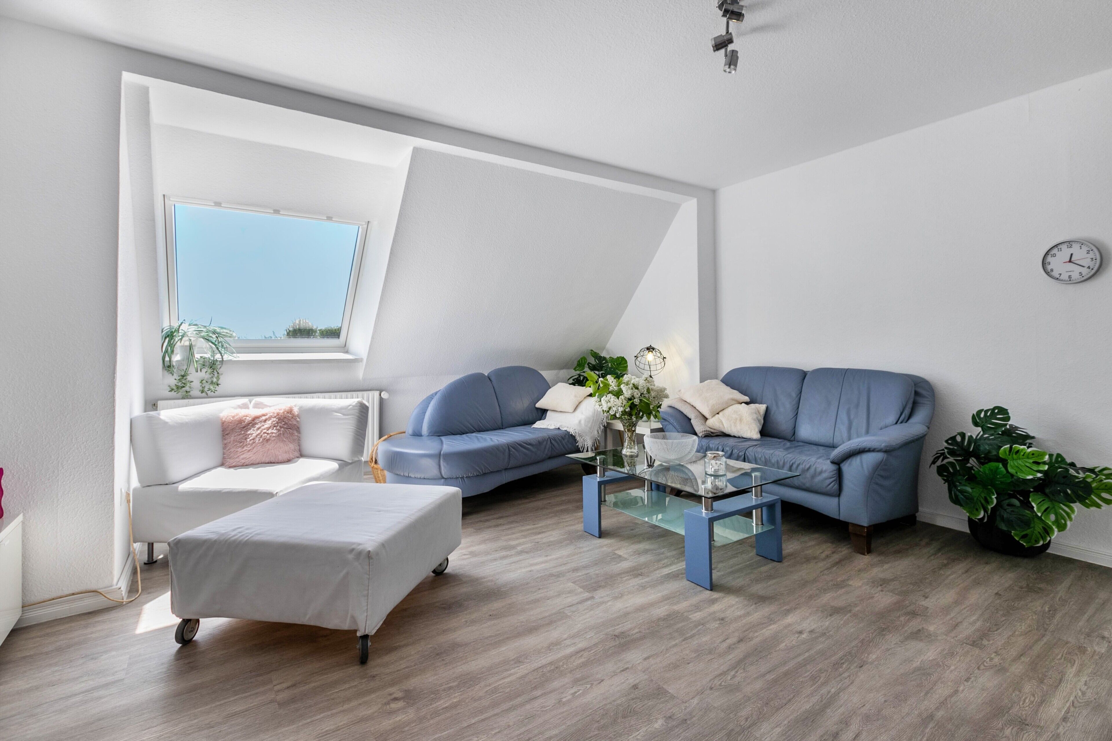 Ein modernes Wohnzimmer mit einem weißen Sofa, einem blauen Sofa, einem Glastisch und einem großen Fenster mit Ausblick.