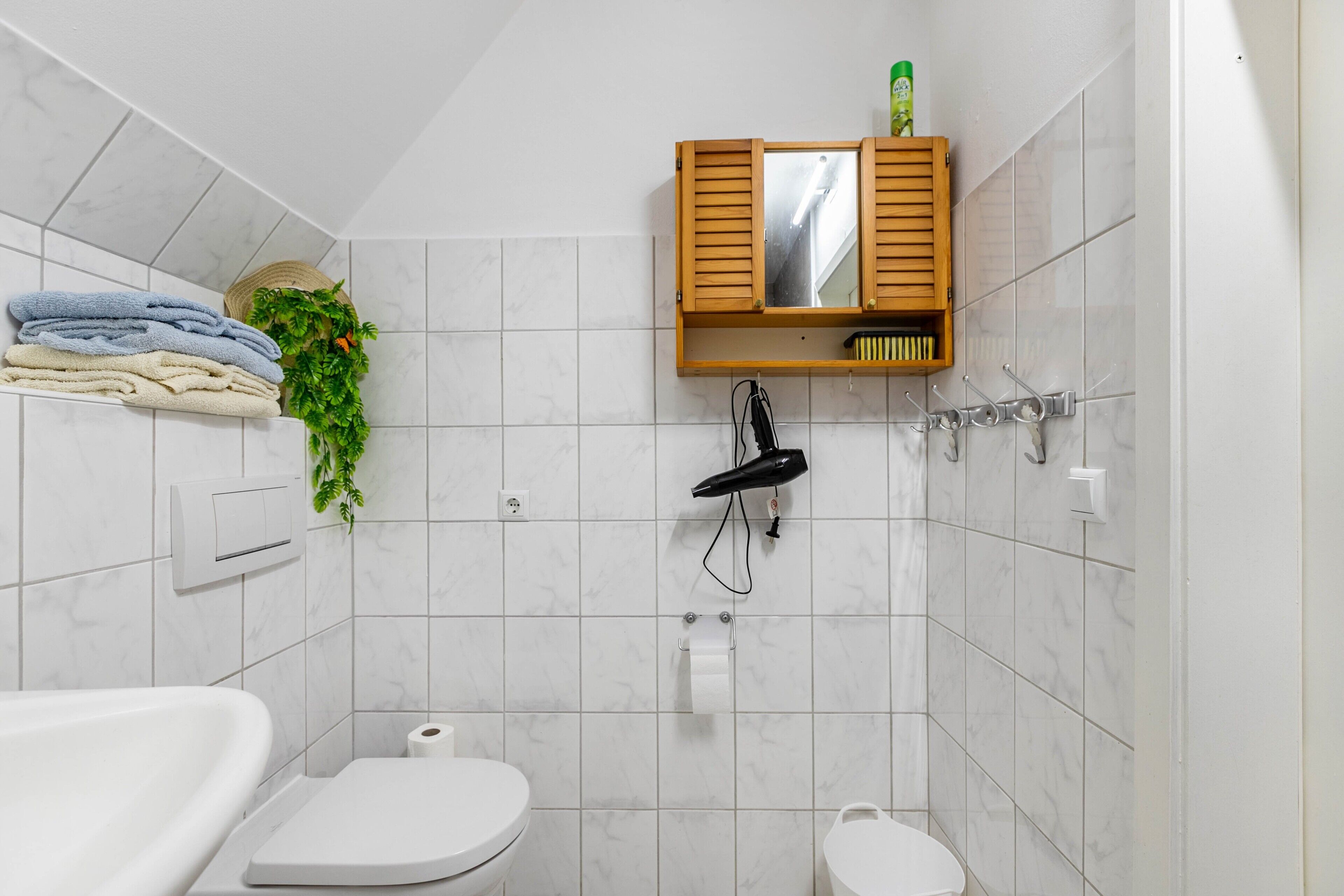 Une salle de bain avec une baignoire blanche, des toilettes, un lavabo, un porte-serviettes avec des serviettes pliées, un sèche-cheveux et un meuble avec miroir.