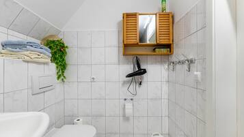 Une salle de bain avec une baignoire blanche, des toilettes, un lavabo, un porte-serviettes avec des serviettes pliées, un sèche-cheveux et un meuble avec miroir.