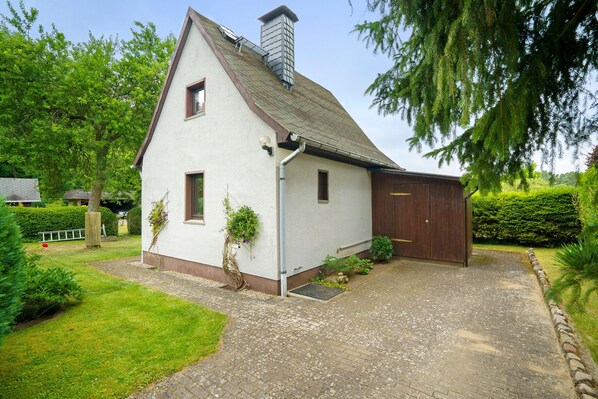 A white house with a brown roof, a chimney, and a wooden garage door.