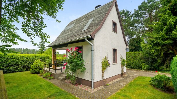 A small, single-story house with a sloped roof, a porch with a bench, and a garden with hedges and flowering plants. - Holiday Home 'Carpin' with Private Terrace, Garden and Wi-Fi (Carpin)
