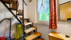 A staircase with wooden steps, a vacuum cleaner, a trash bin, a window with a view of greenery, and a mirror on the wall. - Holiday Home 'Carpin' with Private Terrace, Garden and Wi-Fi (Carpin)