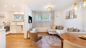 Ein modernes Wohnzimmer mit einer Couch, einem Esstisch und einer Küchenzeile mit Fenster und Vorhängen.