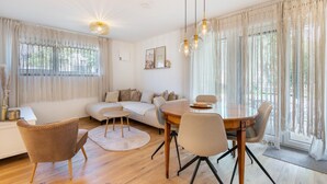 Ein modernes Wohnzimmer mit einer Couch, einem Esstisch, Stühlen und einem großen Fenster mit Vorhängen.