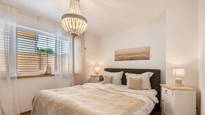 Ein Schlafzimmer mit Bett, Nachttischen, einer Deckenleuchte, einem Fenster mit Jalousien und einem Bild an der Wand.