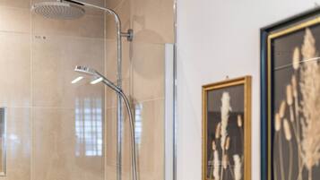 A modern bathroom with a glass shower enclosure, chrome fixtures, and framed artwork on the wall.