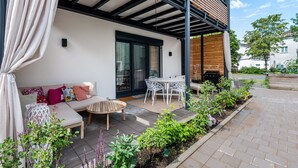 Eine moderne Terrassenanlage mit einer Couch, Sesseln und einem Esstisch.