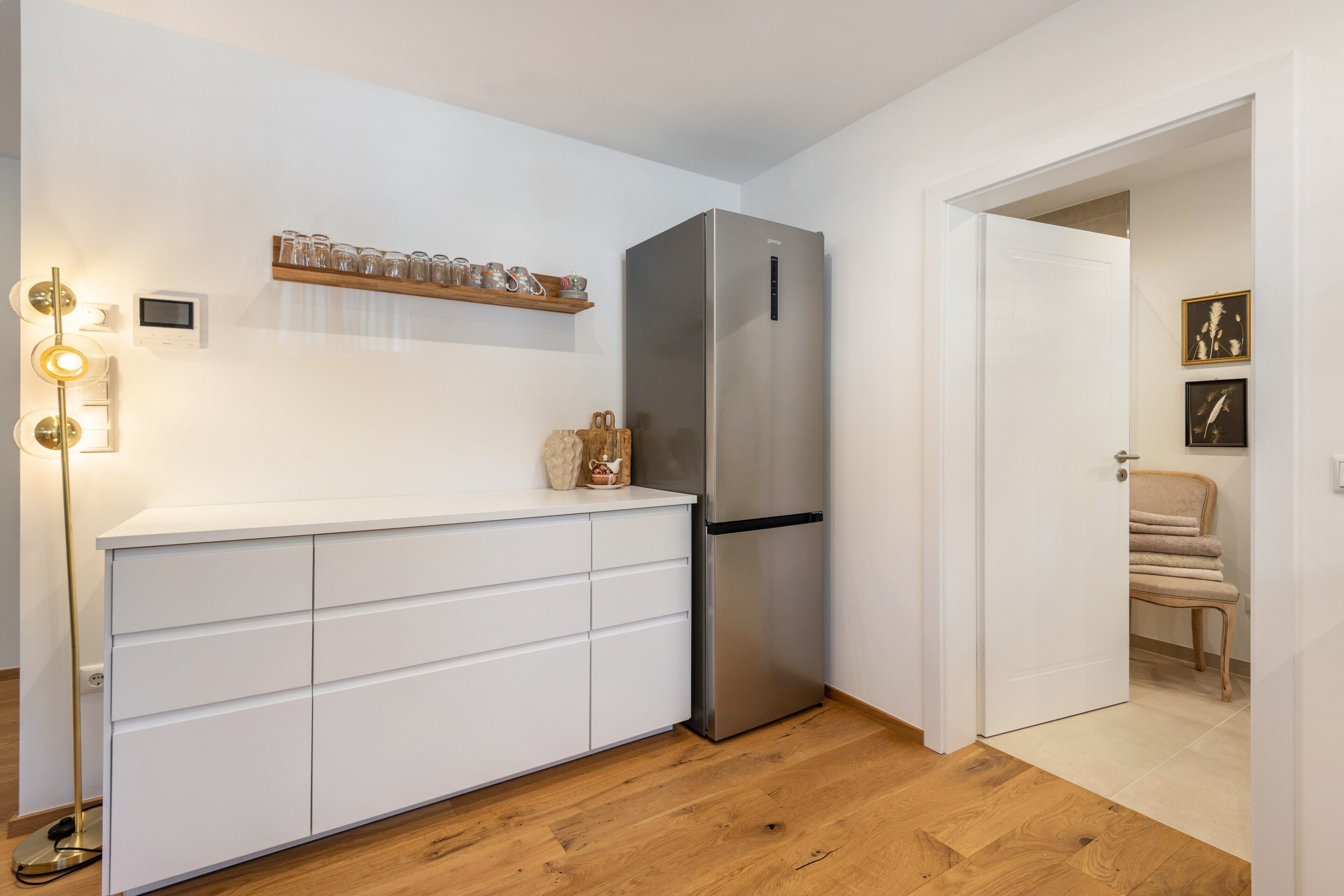Een moderne keuken met een geïntegreerde roestvrijstalen koelkast, witte kastjes en een houten vloer.
