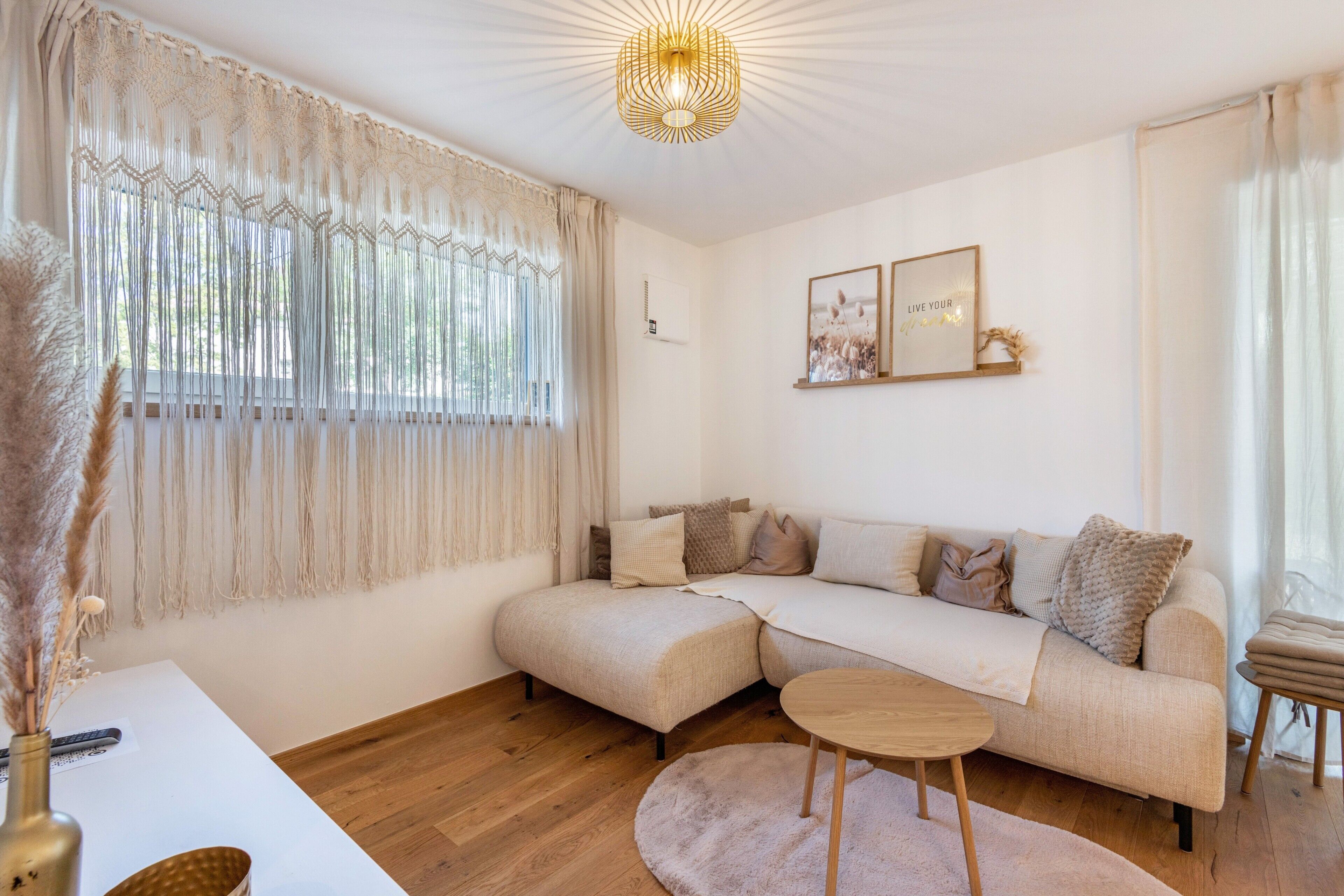 Een moderne woonkamer met een modulaire bank, een ronde houten salontafel en een decoratief macramé gordijn.
