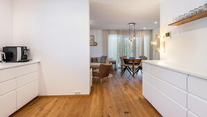 A modern kitchen with white cabinetry, a dining area with a wooden table and chairs, and a visible coffee machine. - Apartment 'Bei Thérèse' with Private Terrace and Wi-Fi (Miltach)