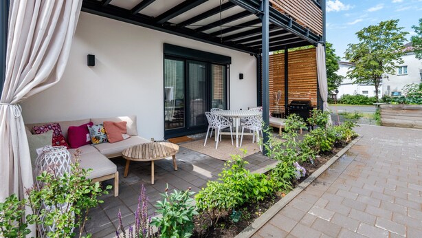 A covered outdoor seating area with a sofa, chairs, and a table, surrounded by plants and a brick pathway. - Apartment 'Bei Thérèse' with Private Terrace and Wi-Fi (Miltach)