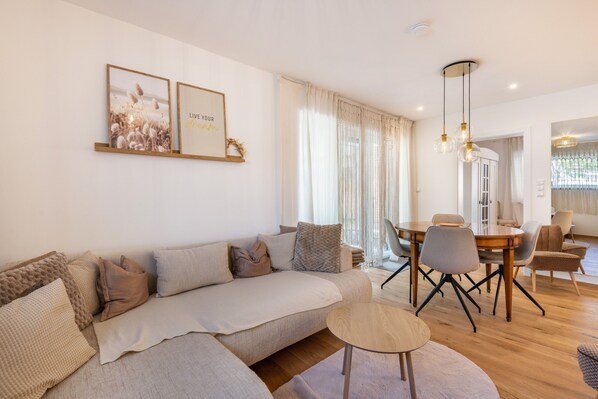 Un salon moderne avec un canapé, une table à manger et des chaises. Les murs sont ornés de tableaux encadrés et un lustre illumine la pièce.