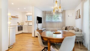 A modern kitchen with white cabinetry, a dining table with chairs, a built-in oven, and a large window with curtains. - Apartment 'Bei Thérèse' with Private Terrace and Wi-Fi (Miltach)
