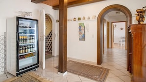 Ein Flur mit einem Kühlschrank voller Getränke, Holzbalken an der Decke, einem gemusterten Teppich und einem Durchgang zu einem weiteren Raum.