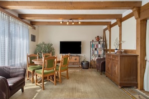 Ein Wohnzimmer mit Holzboden, einem Flachbildfernseher, einem Bücherregal, einem Esstisch mit Stühlen und einem Sofa.