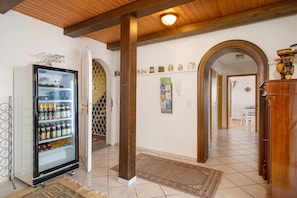 A hallway with a refrigerator stocked with beverages, wooden beams on the ceiling, a patterned rug, and an archway leading to another room.