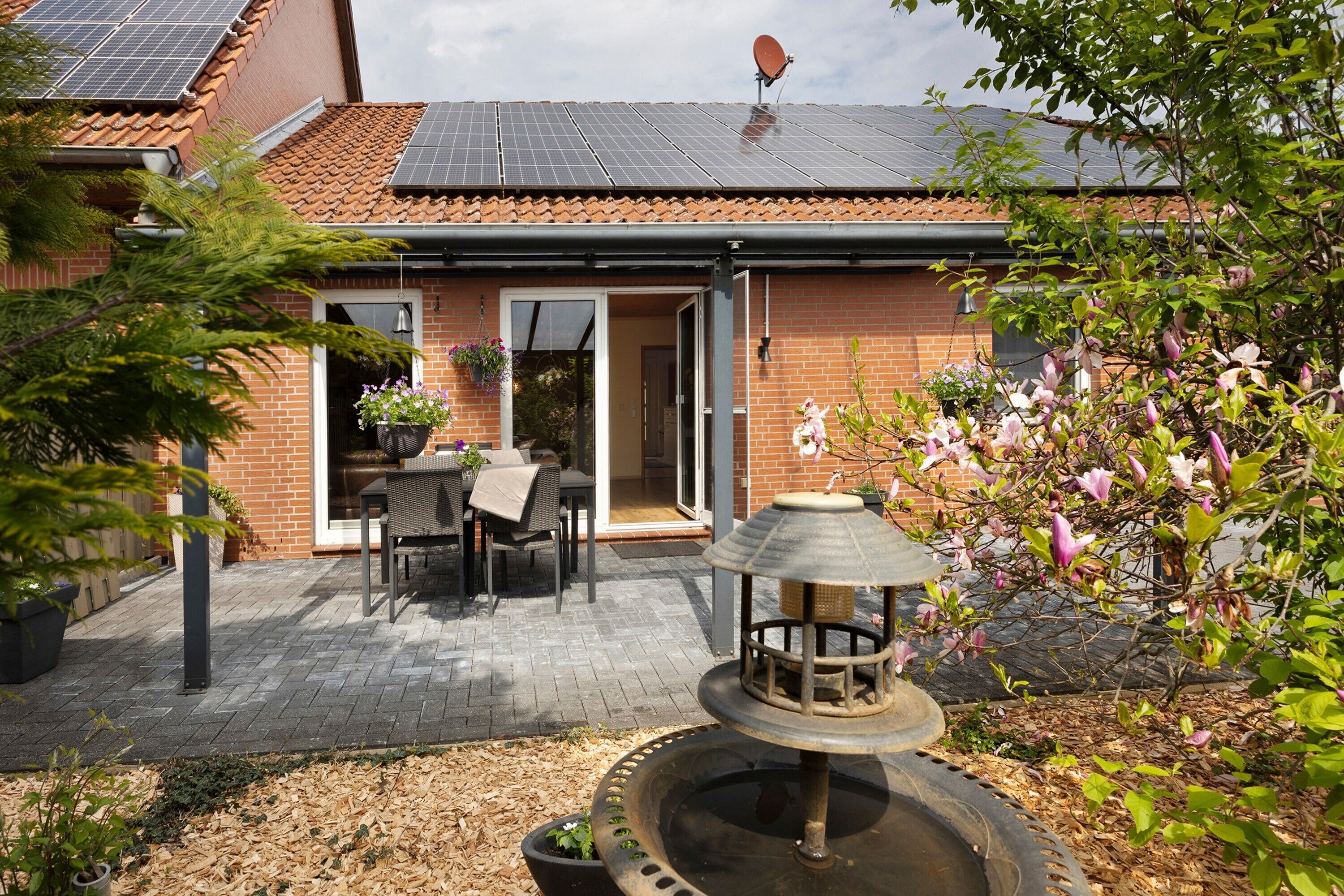 A brick house with a tiled roof, a patio with a table and chairs, and a water feature.