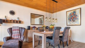 Un comedor con una mesa de madera, sillas, lámparas colgantes, un espejo y un estante con adornos.