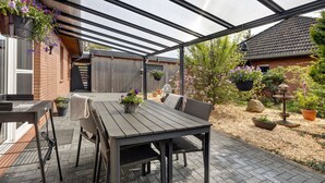 Un patio cubierto con una mesa, sillas, plantas en macetas y una pared de ladrillo.