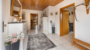 Un pasillo con techo de madera, un espejo, un jarrón con flores, un tapete y una puerta que da a otra habitación.