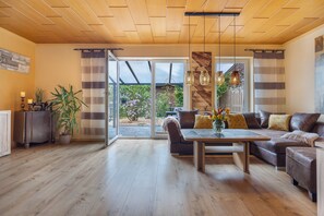 Een moderne woonkamer met een houten plafond, een zithoek, een eettafel en een grote schuifpui naar een tuin.