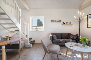 A modern living room with a staircase, a sofa, a coffee table, and a vase of flowers. - Holiday Home 'Helgohuus' with Private Terrace, Private Garden and Wi-Fi (Wöhrden)