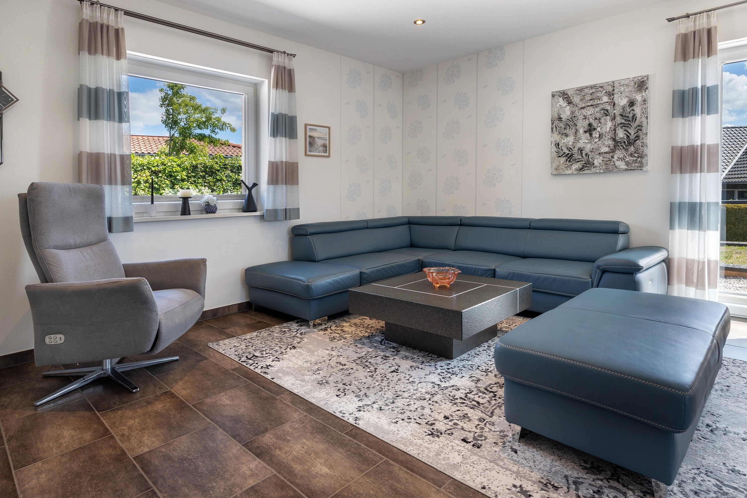 Uma sala de estar moderna com uma poltrona cinza, um sofá modular azul, uma mesa de centro e um tapete estampado.