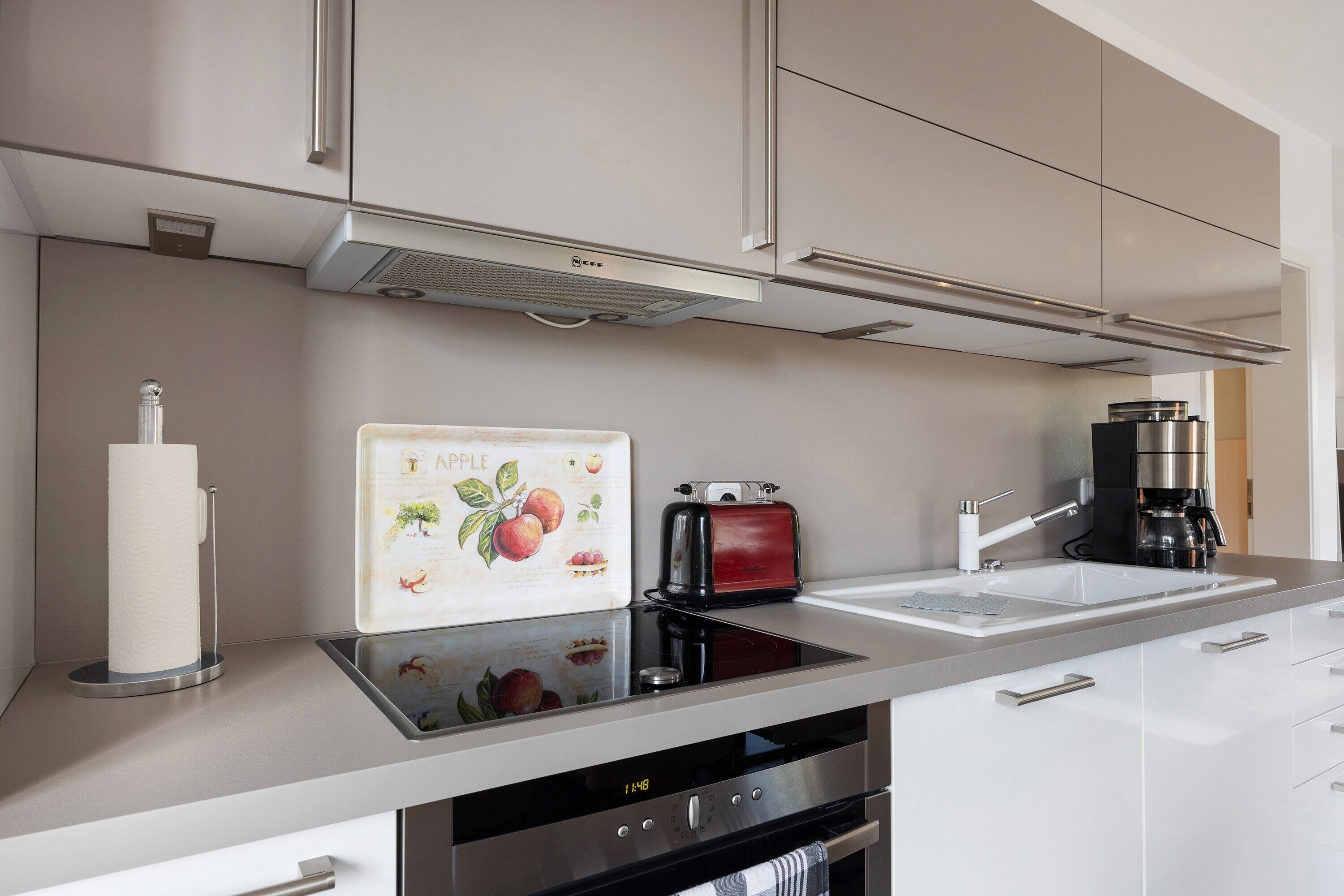 A modern kitchen with a built-in oven, a toaster, a coffee maker, and a paper towel holder.