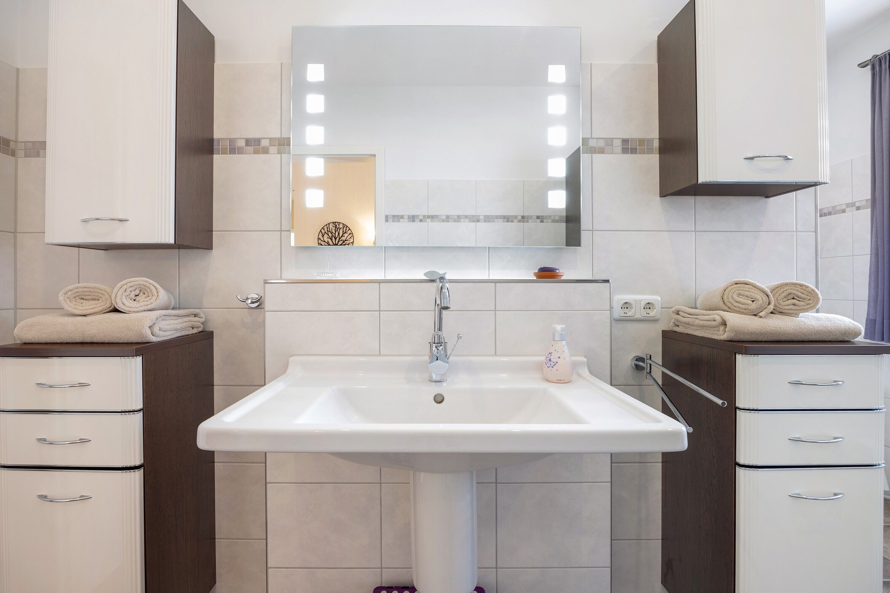 A bathroom with a white sink, mirror, and two towel racks.