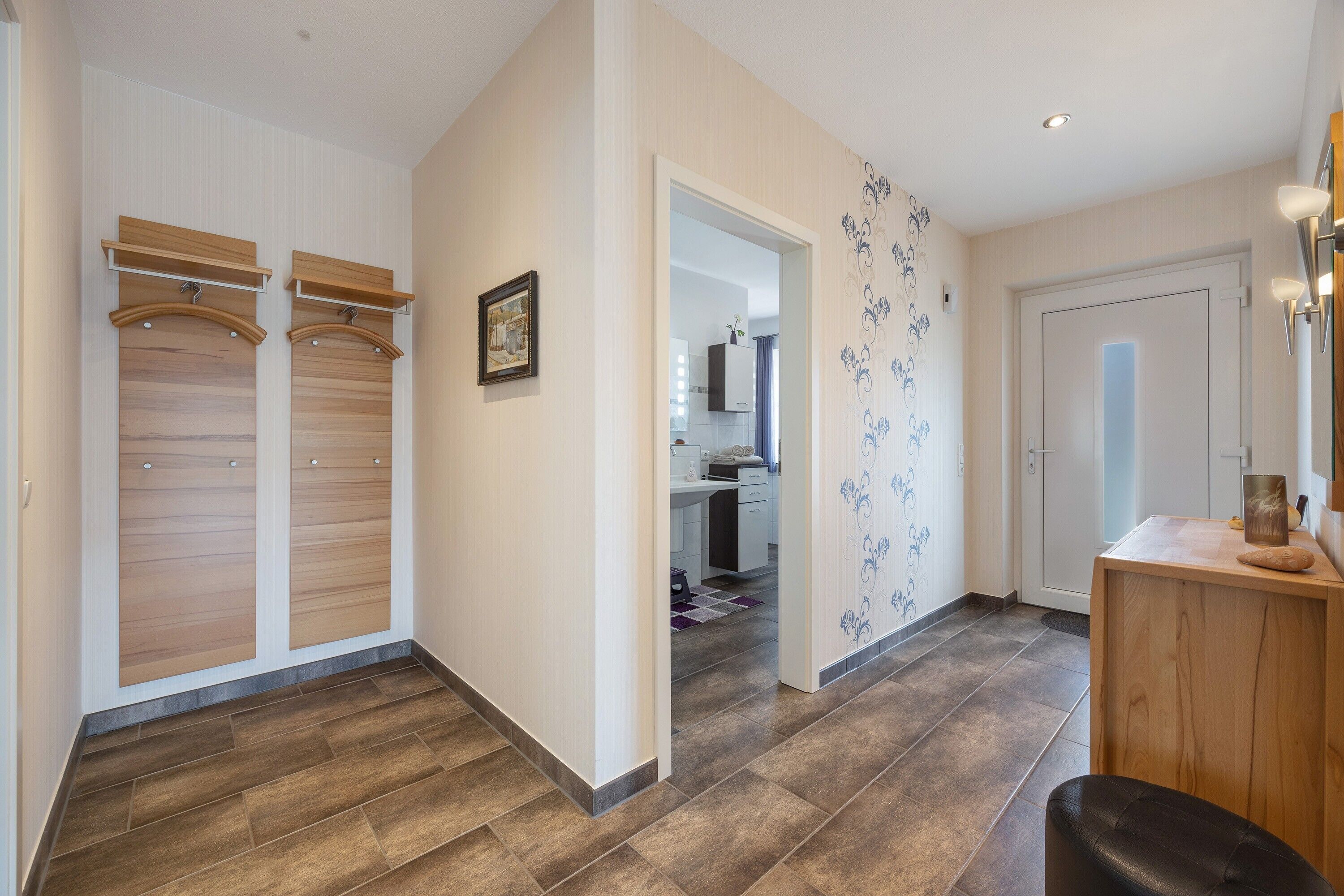 Un couloir avec un banc en bois, une porte et une étagère fixée au mur.