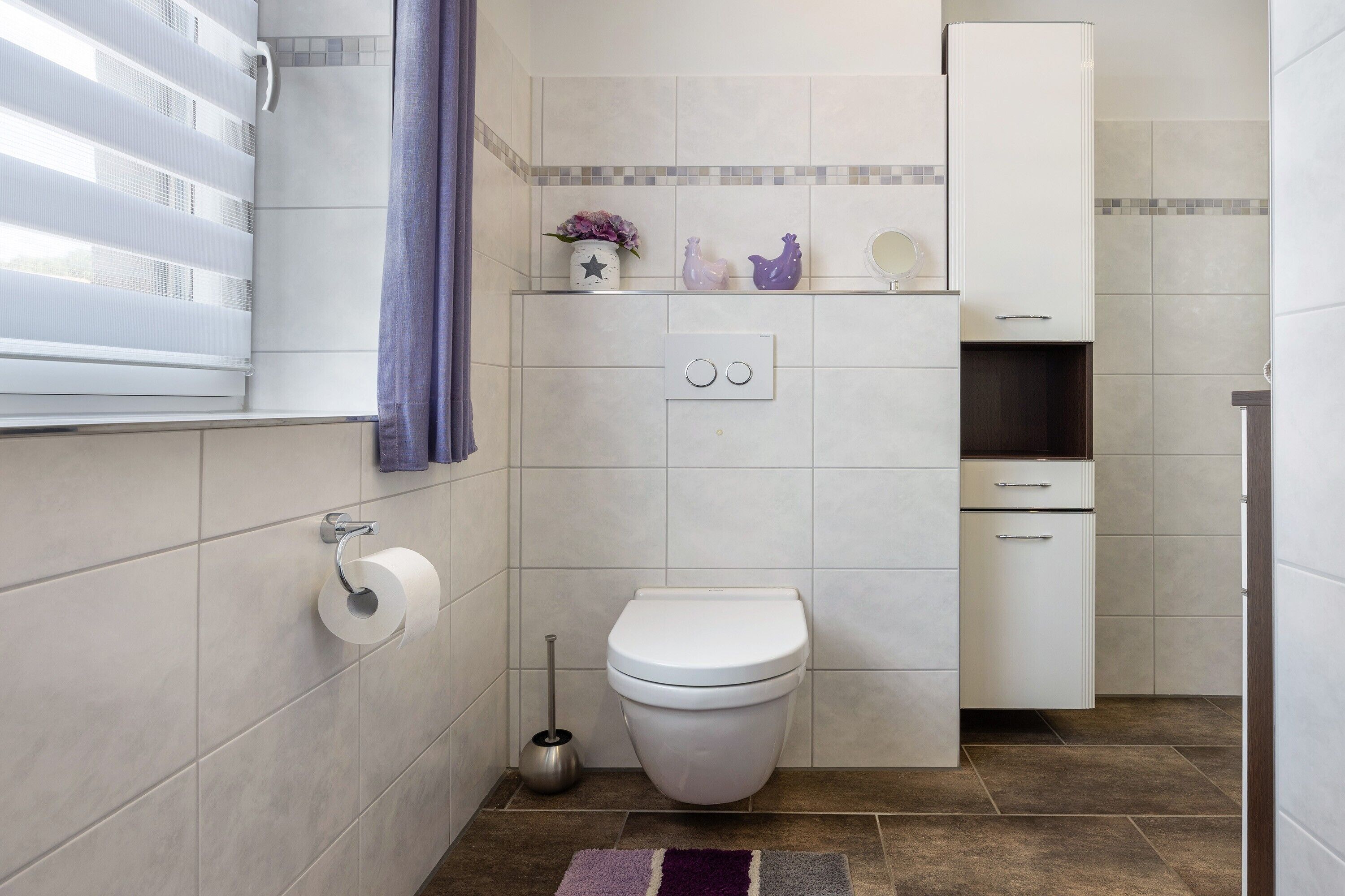 A bathroom with a toilet, a bidet, a towel rack, a mirror, and a shelf with decorative items.