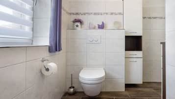 A bathroom with a toilet, a bidet, a towel rack, a mirror, and a shelf with decorative items.
