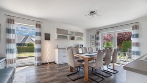 A modern dining area with a table and chairs, a kitchen in the background, and large windows with curtains. - Apartment 'Sunny' with Private Terrace, Private Garden and Wi-Fi (Beckdorf)