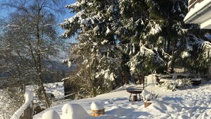 Een besneeuwde buitenruimte met een houten hek, sneeuw bedekte bomen en een metalen tafel.