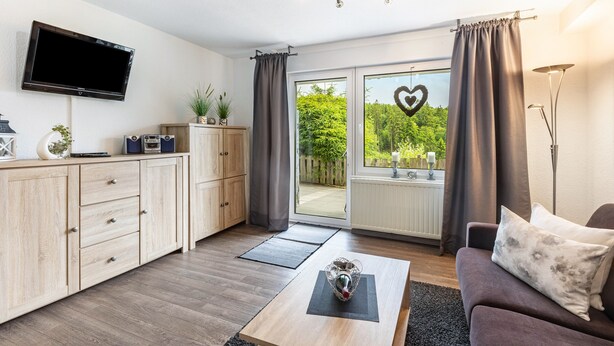 Een moderne woonkamer met een flatscreen televisie, houten kasten, een bank en een grote schuifpui naar buiten.
